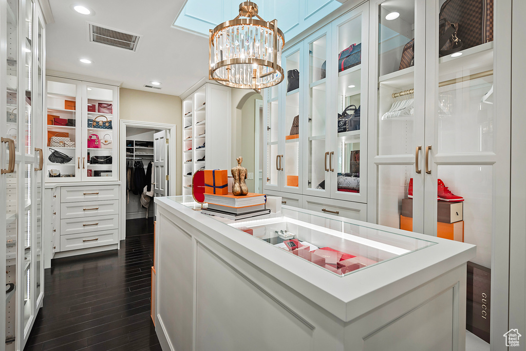 Spacious closet with dark wood finished floors and a chandelier