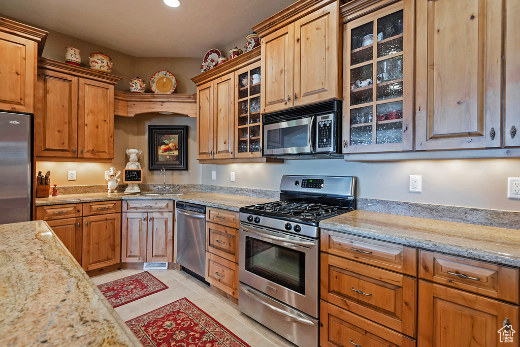 Kitchen featuring stainless steel appliances, a sink, light tile patterned floors, light stone counters, and recessed lighting