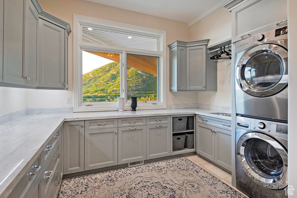 Laundry room featuring cabinet space, stacked washer / drying machine, light tile patterned flooring, and ornamental molding