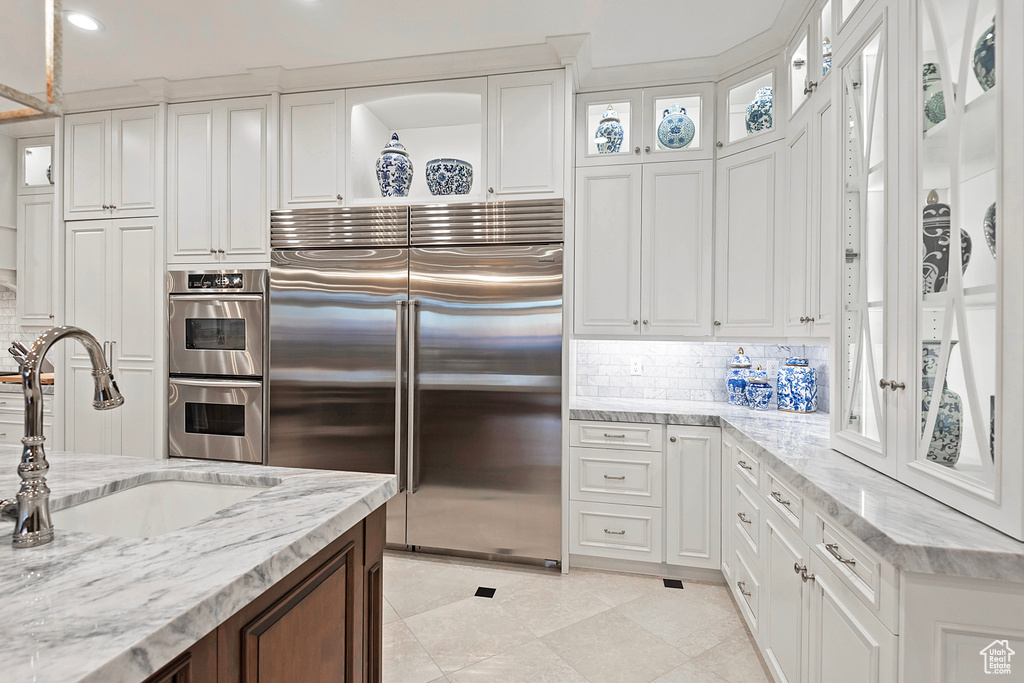 Kitchen featuring appliances with stainless steel finishes, a sink, white cabinetry, tasteful backsplash, and light stone countertops