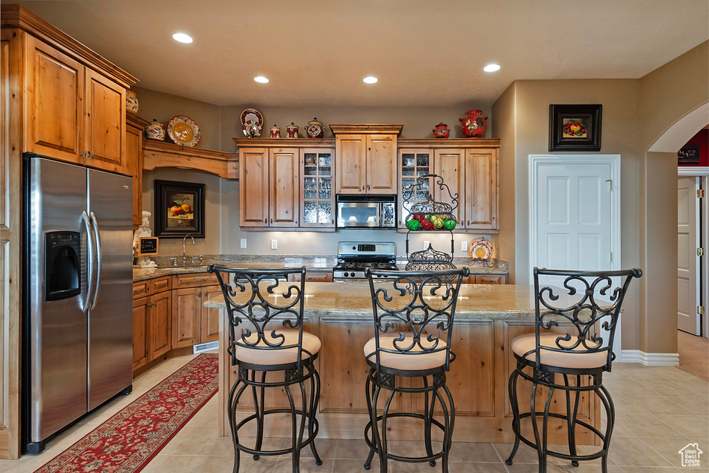 Kitchen with appliances with stainless steel finishes, arched walkways, recessed lighting, light tile patterned floors, and glass insert cabinets