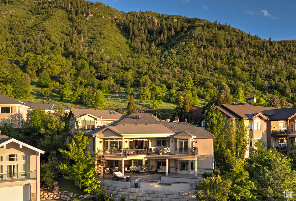 Back of property featuring a wooded view, a patio, a balcony, and a mountain view