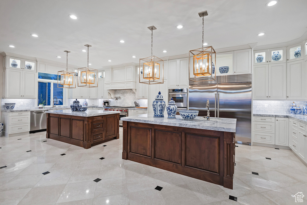Kitchen featuring a center island with sink, premium appliances, tasteful backsplash, a chandelier, and recessed lighting