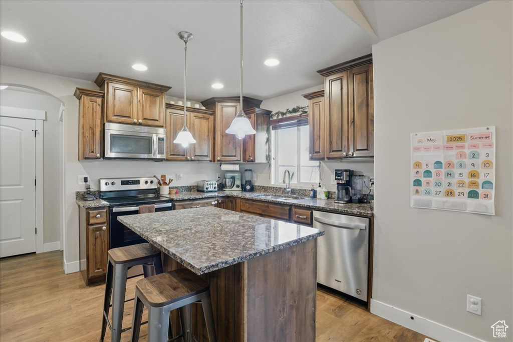 Kitchen with appliances with stainless steel finishes, a sink, light wood-style flooring, arched walkways, and a breakfast bar area