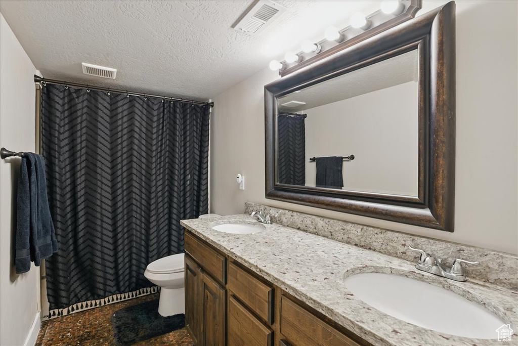 Full bathroom with double vanity, toilet, a textured ceiling, and curtained shower