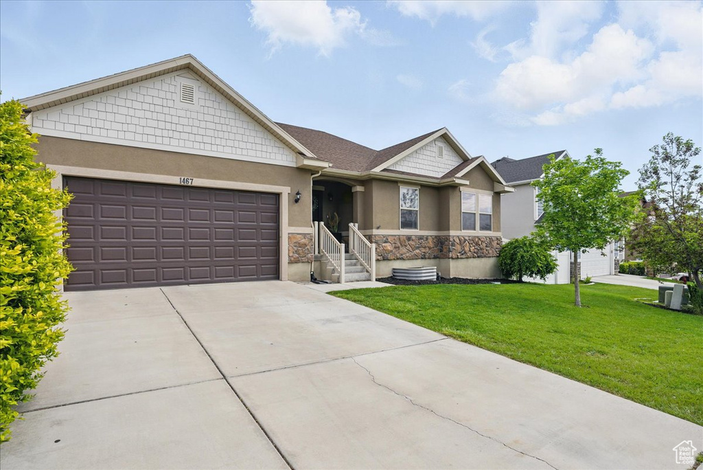 View of front of home featuring stucco siding, stone siding, an attached garage, a front yard, and concrete driveway