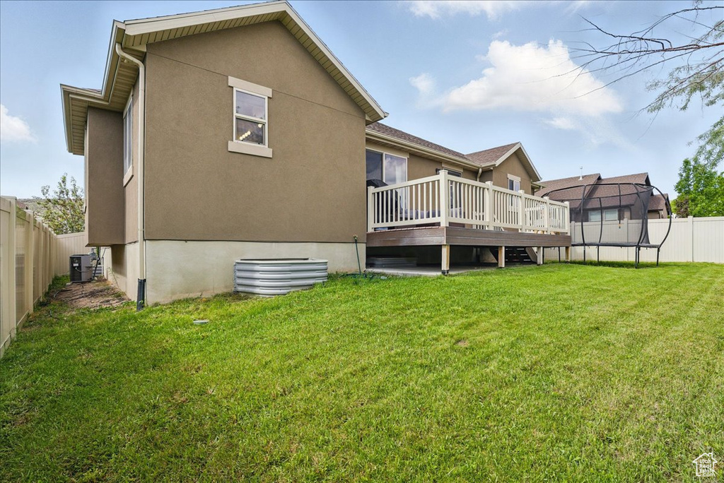 Back of house with a wooden deck, a trampoline, stucco siding, and central AC unit