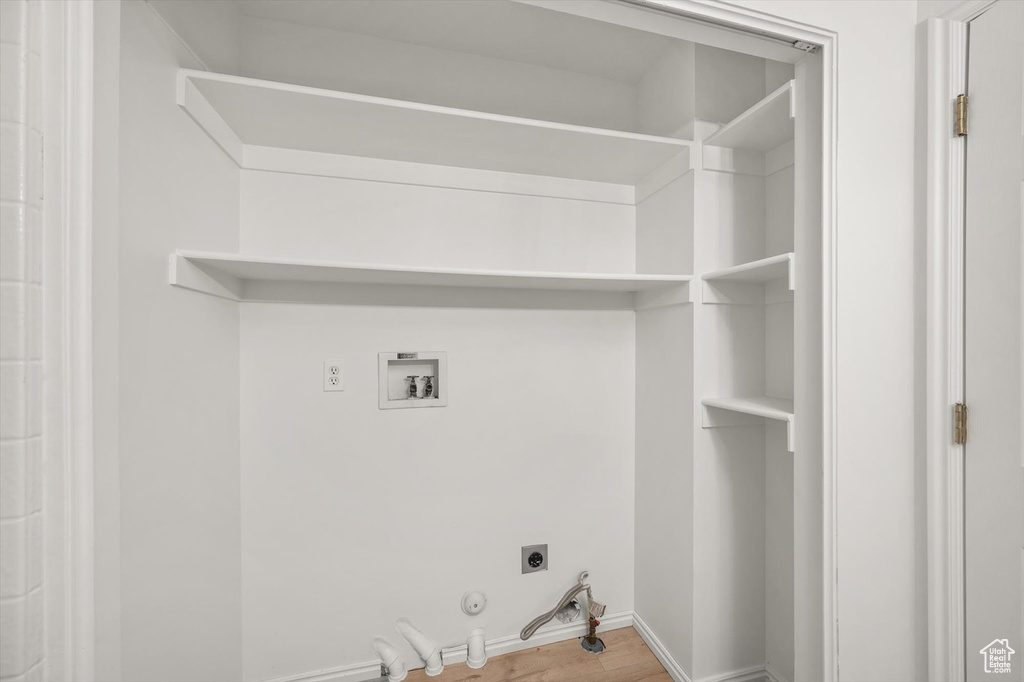 Washroom with hookup for an electric dryer, hookup for a gas dryer, hookup for a washing machine, wood finished floors, and baseboards