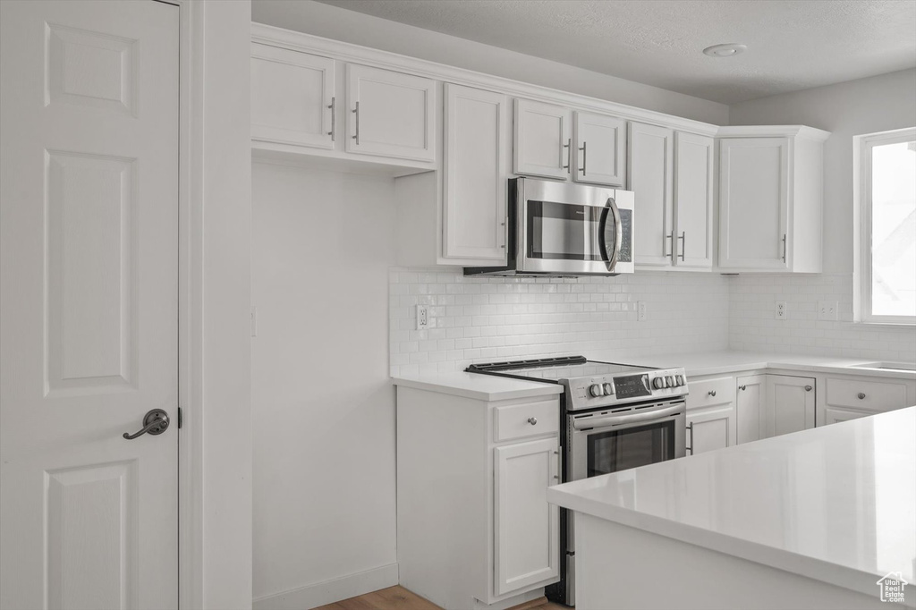 Kitchen with stainless steel appliances, decorative backsplash, light countertops, and white cabinets