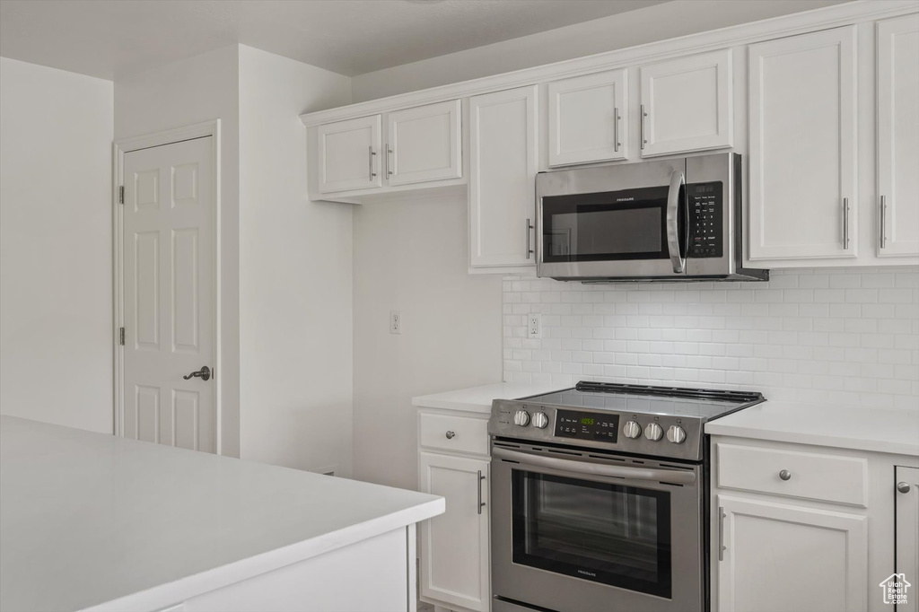 Kitchen featuring appliances with stainless steel finishes, light countertops, decorative backsplash, and white cabinetry