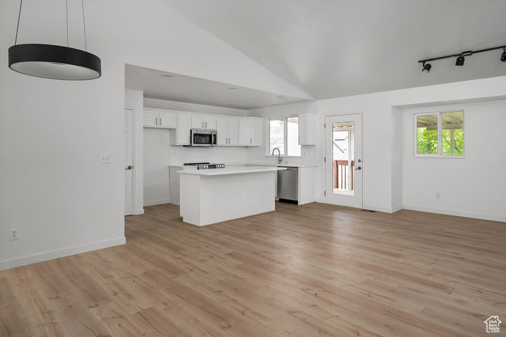 Kitchen with appliances with stainless steel finishes, white cabinetry, open floor plan, light countertops, and lofted ceiling
