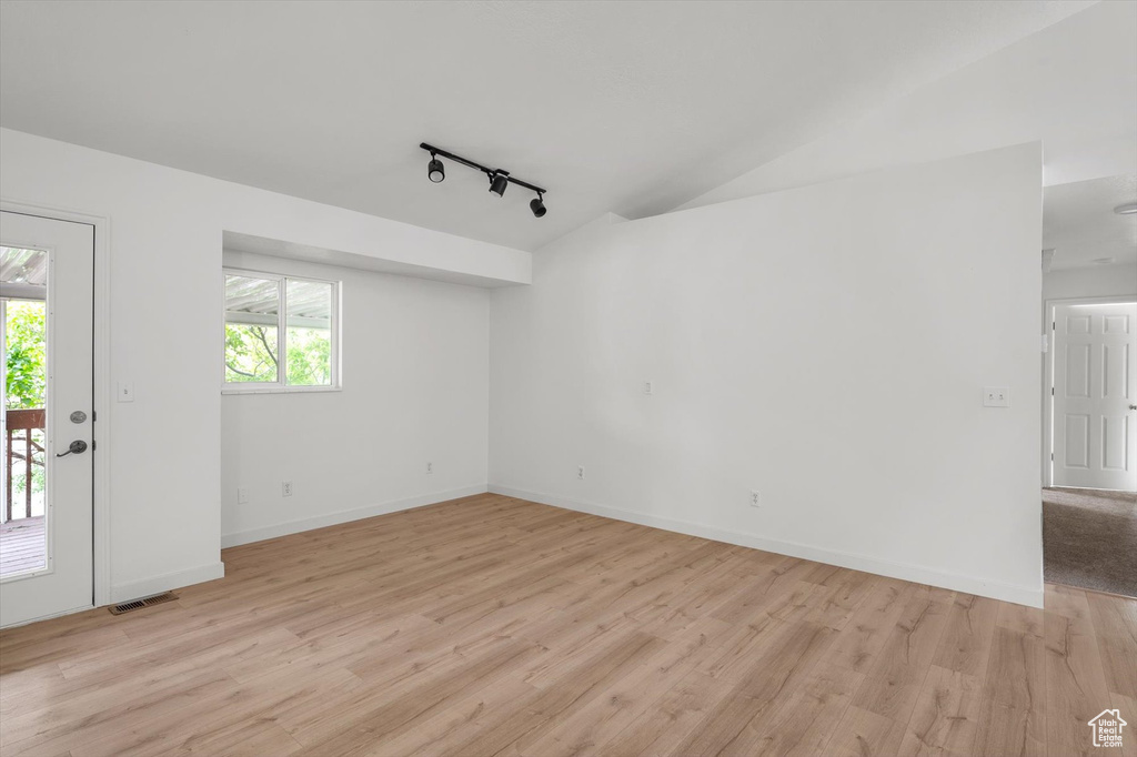Unfurnished room with rail lighting, light wood-type flooring, lofted ceiling, and baseboards