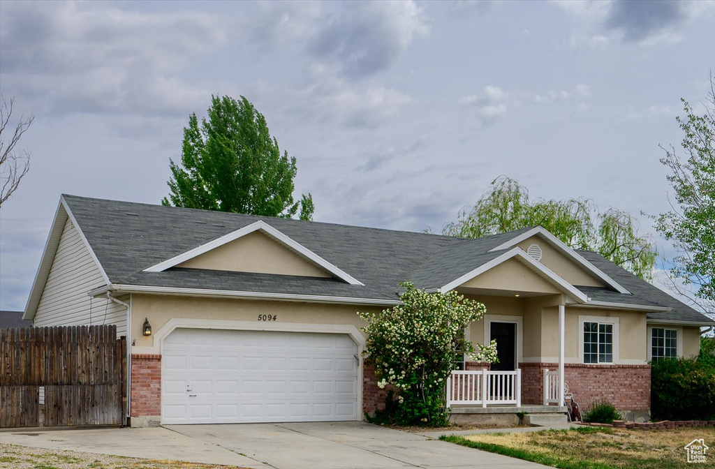Single story home featuring brick siding, a porch, an attached garage, concrete driveway, and stucco siding