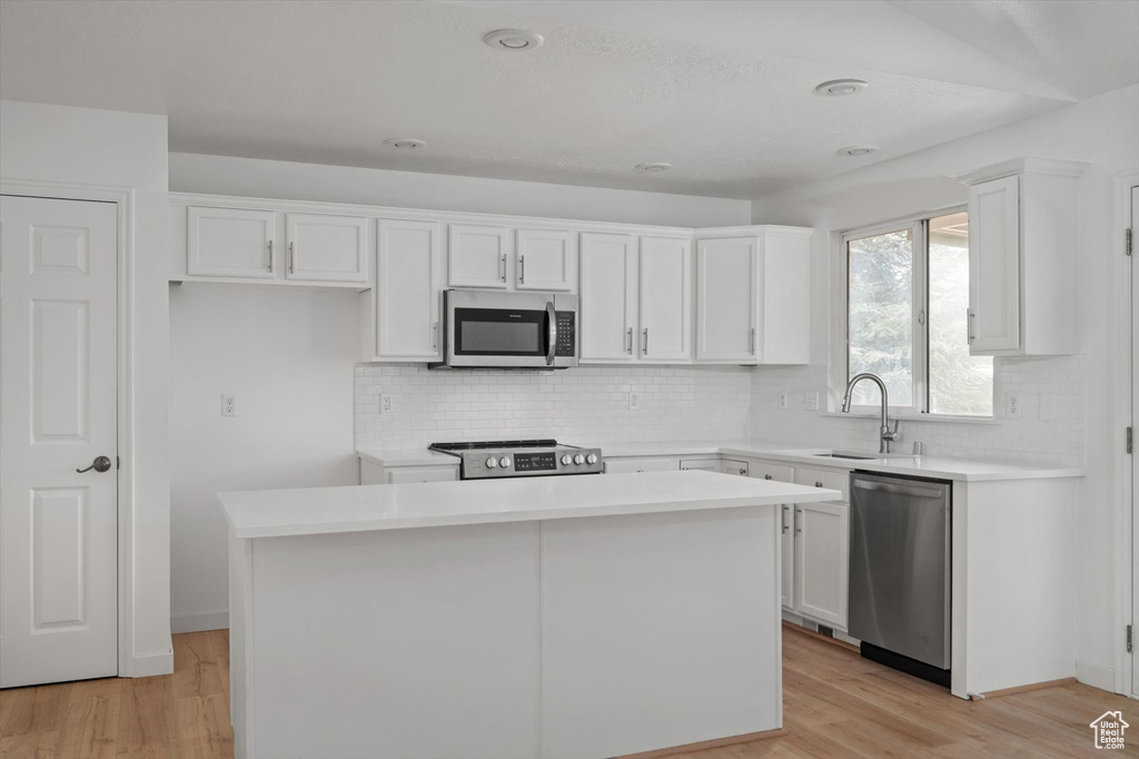 Kitchen featuring appliances with stainless steel finishes, a sink, a kitchen island, white cabinets, and light wood finished floors