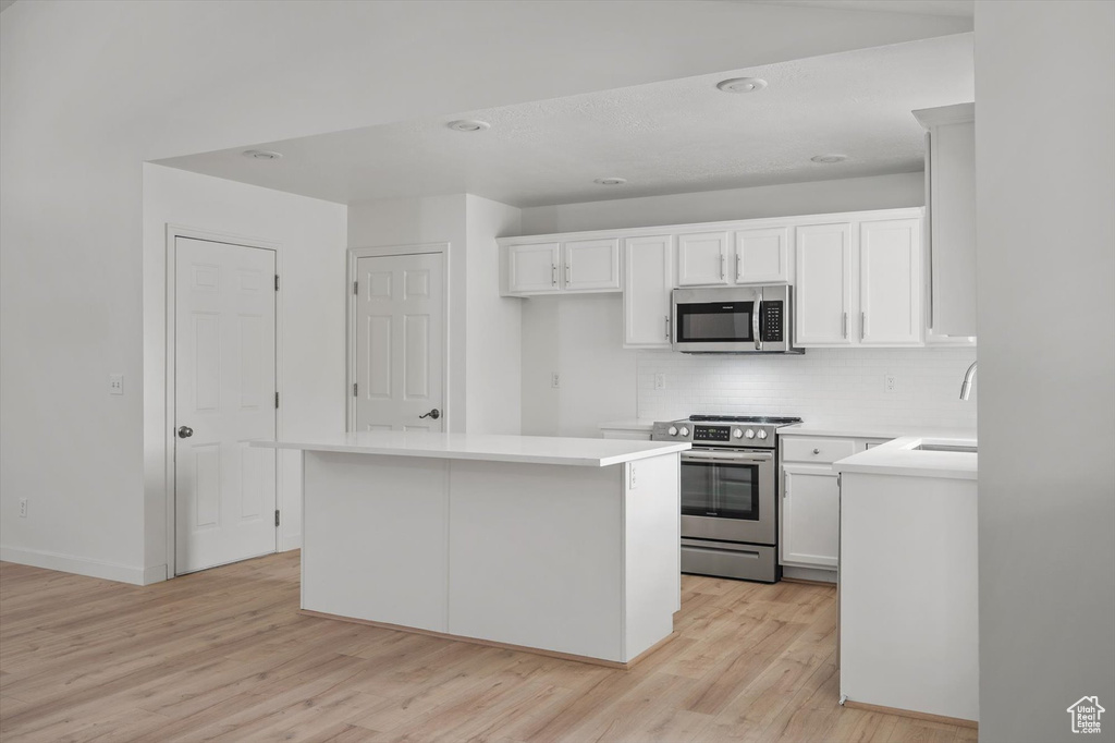 Kitchen with appliances with stainless steel finishes, decorative backsplash, light wood-style flooring, white cabinets, and recessed lighting