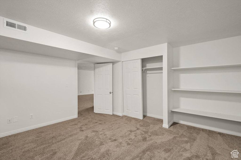 Unfurnished bedroom with carpet, a textured ceiling, baseboards, and a closet