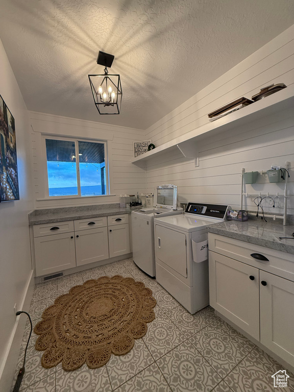 Laundry area with washer and dryer, cabinet space, a textured ceiling, a chandelier, and light tile patterned floors