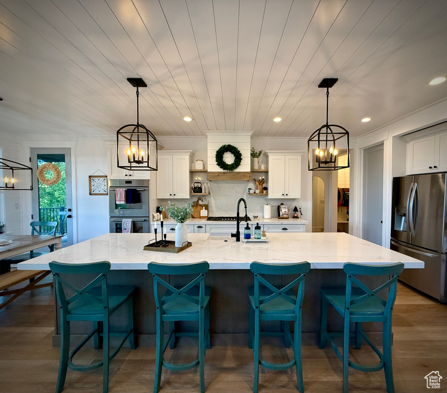 Kitchen with stainless steel refrigerator with ice dispenser, a chandelier, a sink, white cabinetry, and light stone countertops