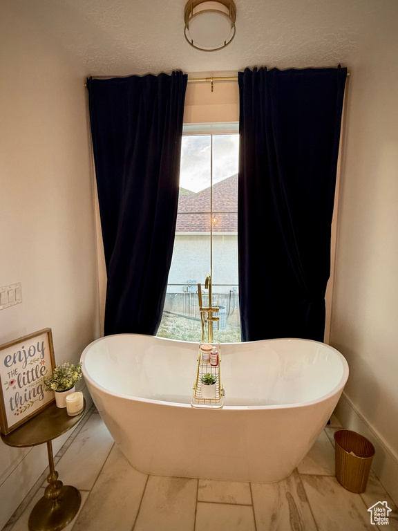 Full bathroom featuring marble look tile flooring, a freestanding bath, and baseboards