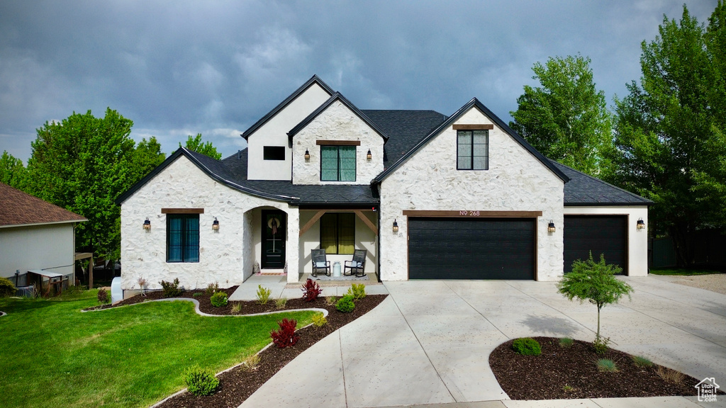 View of front of property featuring a porch, stone siding, a front lawn, driveway, and stucco siding