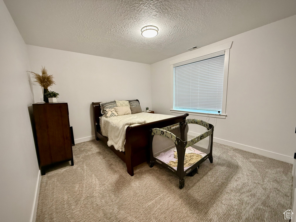 Bedroom featuring a textured ceiling, light carpet, and baseboards