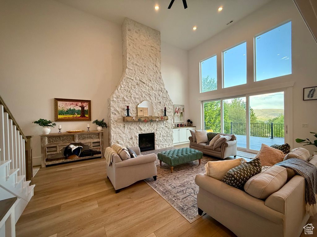 Living room featuring a towering ceiling, light wood-style flooring, a stone fireplace, stairway, and recessed lighting