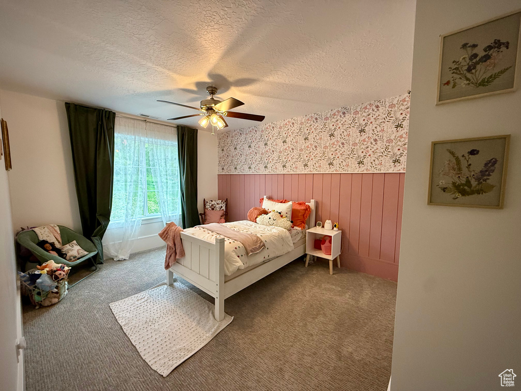 Bedroom featuring wainscoting, a textured ceiling, wallpapered walls, carpet floors, and a ceiling fan