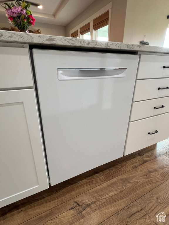 Kitchen view of white dishwasher, white cabinetry, dark wood-style flooring, and light stone countertops