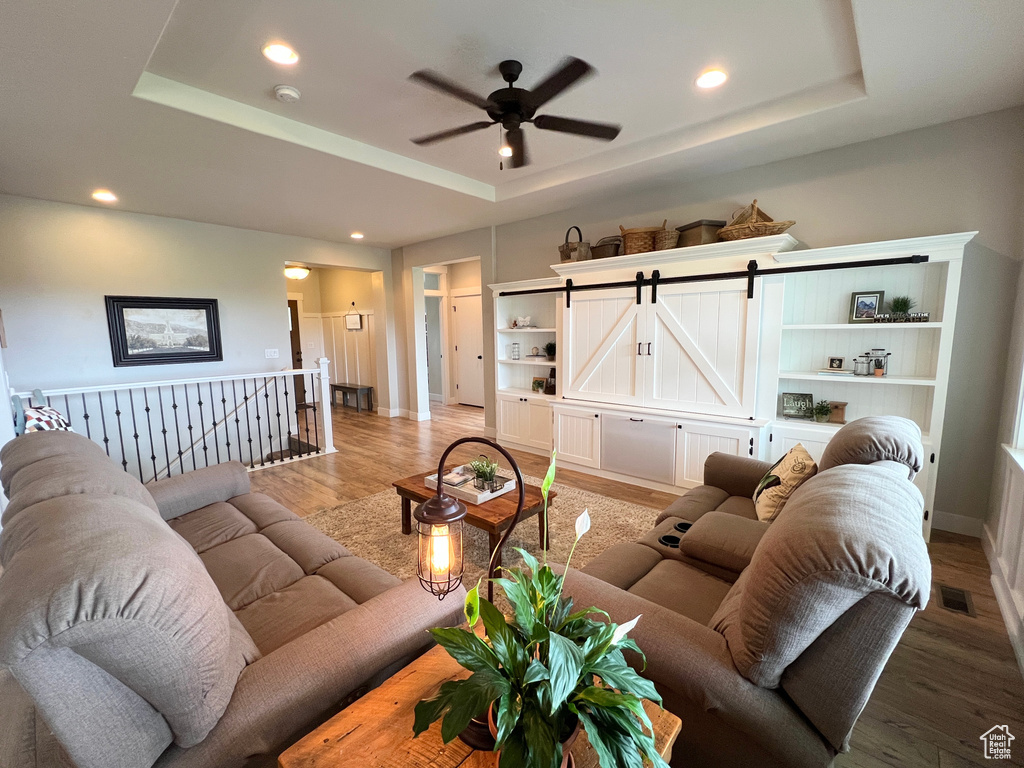 Living room featuring a tray ceiling, baseboards, light wood-type flooring, a ceiling fan, and recessed lighting