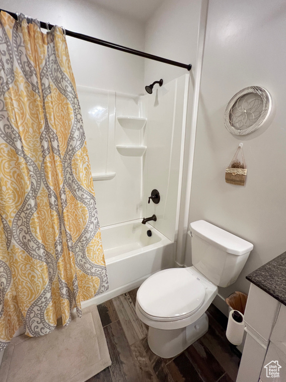Bathroom with wood finished floors, shower / bathtub combination with curtain, vanity, and toilet