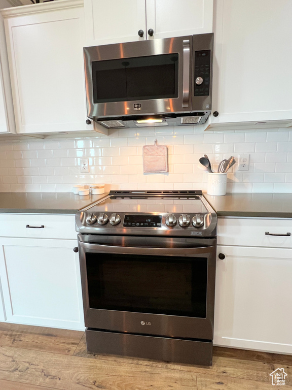 Kitchen featuring appliances with stainless steel finishes, white cabinets, light wood-style floors, and tasteful backsplash