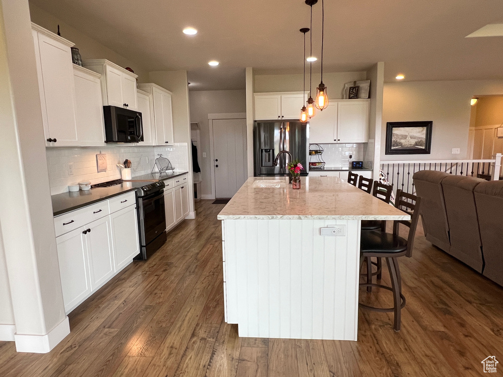 Kitchen featuring stainless steel fridge, black range with electric stovetop, tasteful backsplash, a sink, and white cabinetry