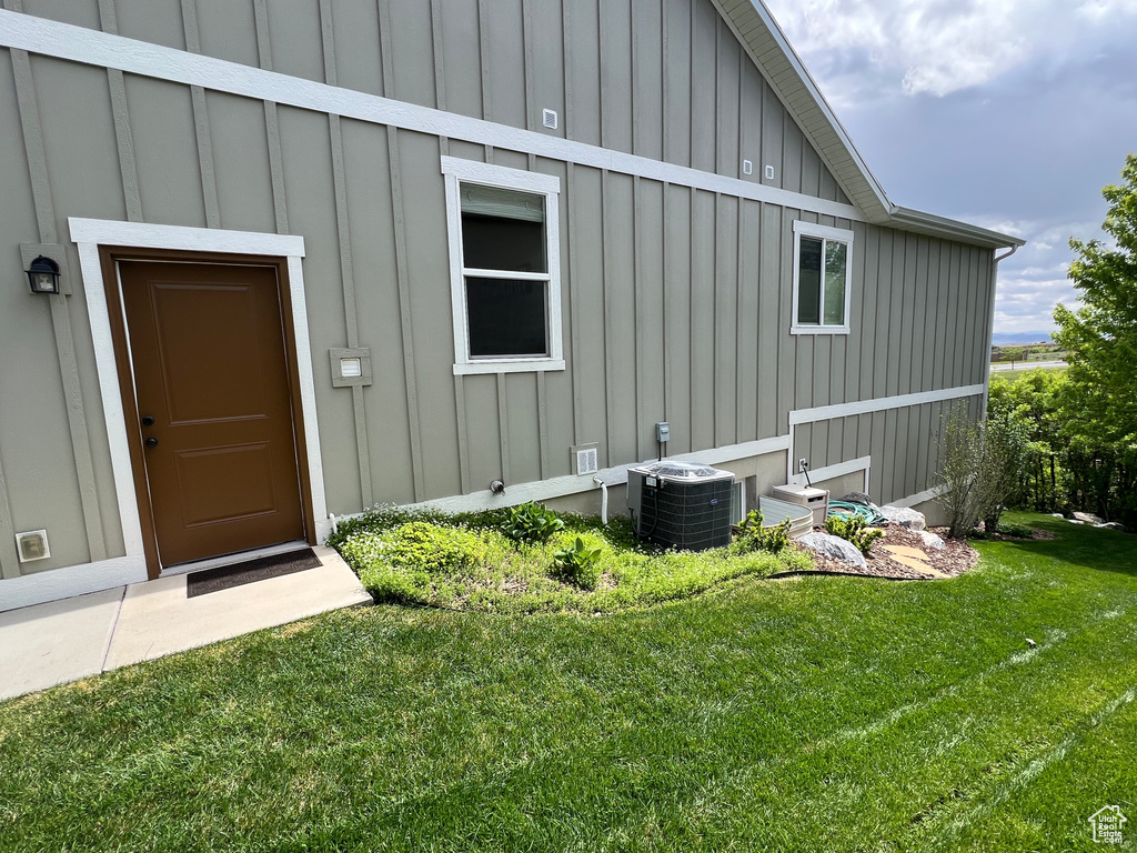 Entrance to property featuring board and batten siding, cooling unit, and a yard