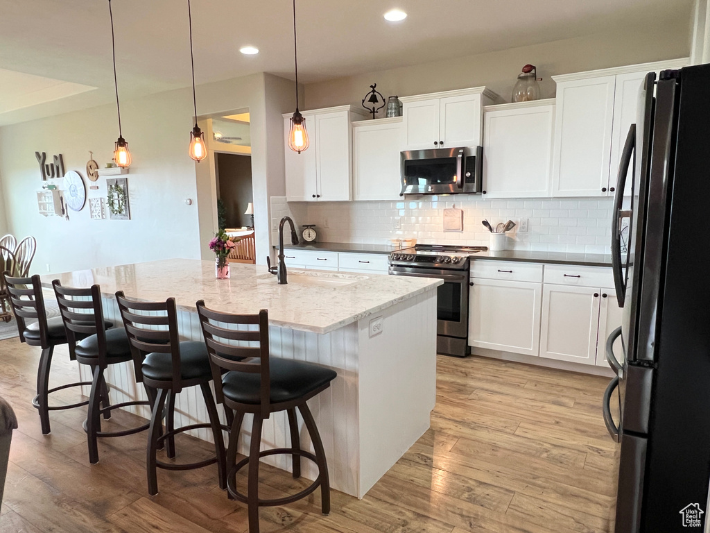 Kitchen with appliances with stainless steel finishes, a sink, decorative backsplash, light wood-style floors, and white cabinets