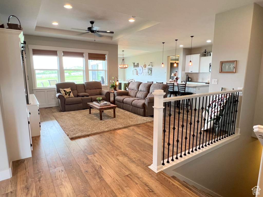 Living area with light wood-type flooring, a raised ceiling, a ceiling fan, and recessed lighting