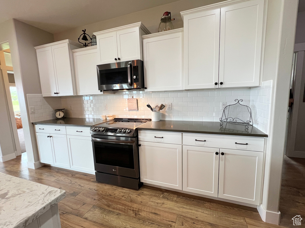 Kitchen with stainless steel appliances, light wood-style floors, white cabinets, backsplash, and dark countertops