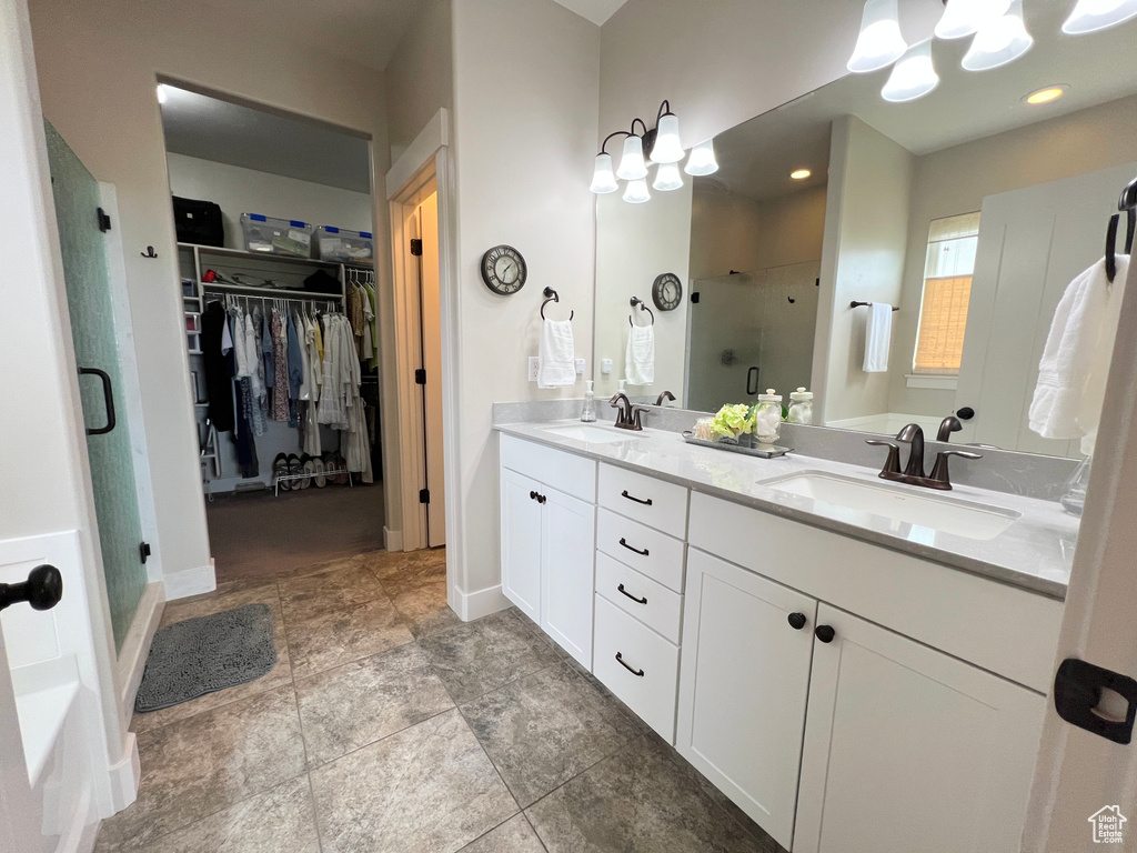 Full bath with a stall shower, double vanity, a walk in closet, baseboards, and a chandelier