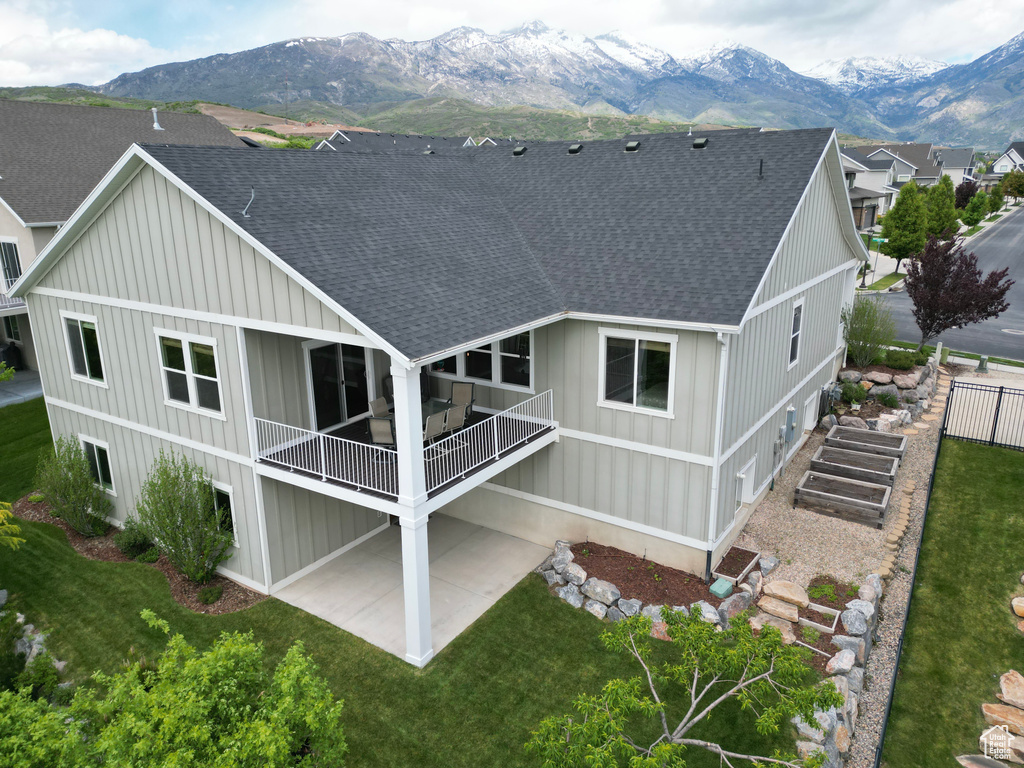 Back of property featuring a shingled roof, a mountain view, board and batten siding, a patio, and a balcony
