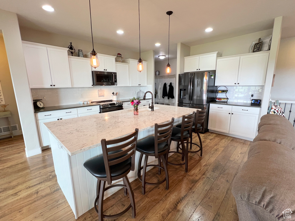 Kitchen featuring stainless steel microwave, black refrigerator with ice dispenser, range with electric stovetop, light wood-type flooring, and decorative backsplash