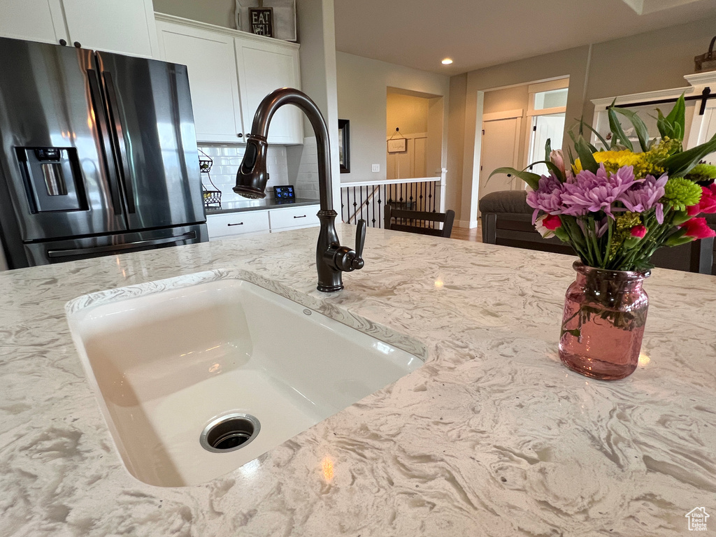 Kitchen view of stainless steel fridge, a sink, backsplash, light stone counters, and recessed lighting