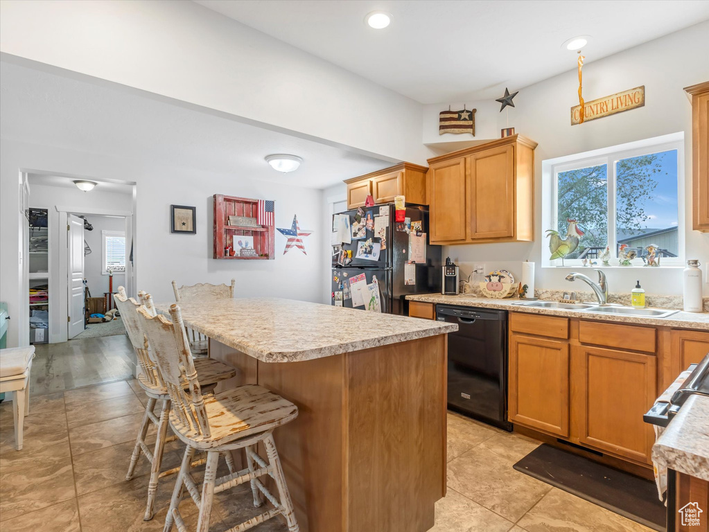 Kitchen featuring black appliances, a sink, light countertops, a breakfast bar area, and recessed lighting