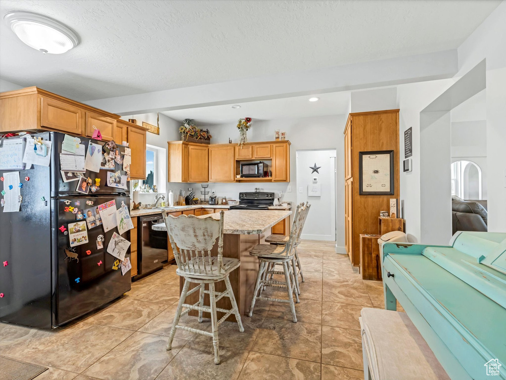 Kitchen featuring black appliances, open floor plan, a kitchen island, a breakfast bar, and recessed lighting