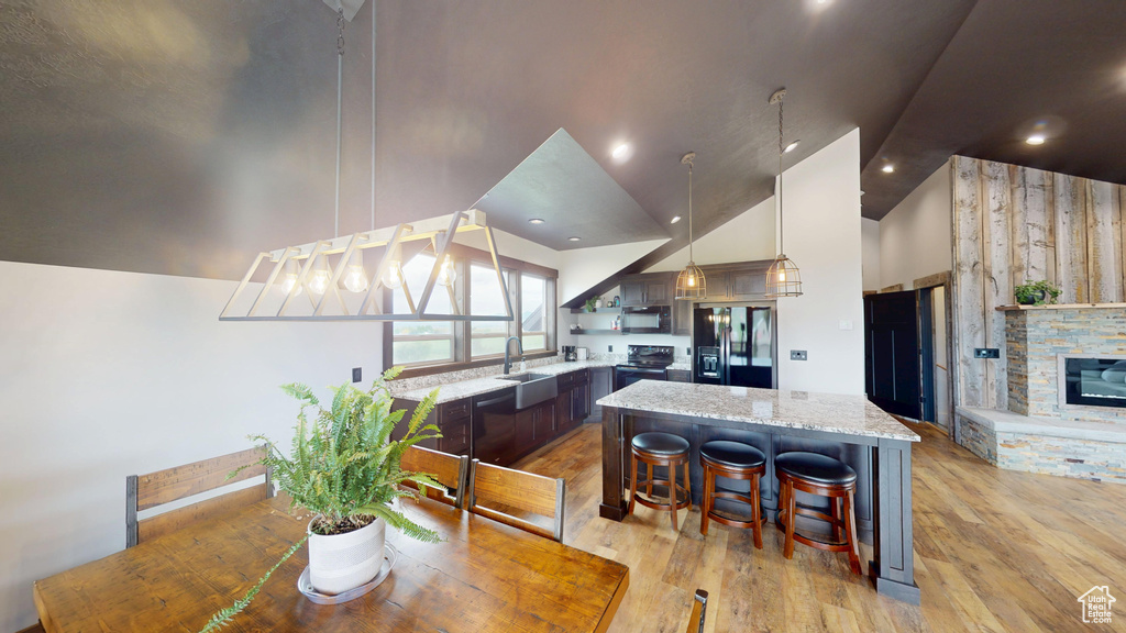 Dining area featuring vaulted ceiling, light wood-style flooring, and a stone fireplace