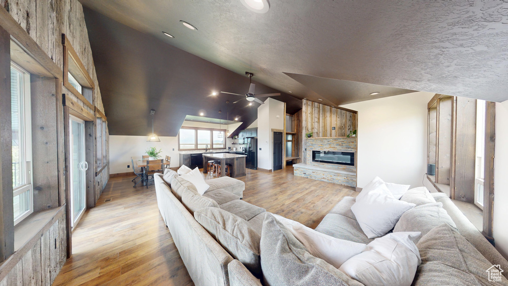 Living room with vaulted ceiling, light wood-type flooring, a stone fireplace, ceiling fan, and baseboards