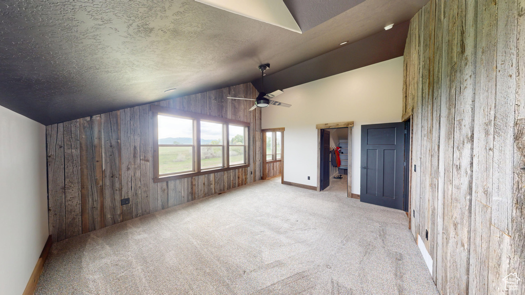 Unfurnished bedroom with lofted ceiling, wooden walls, carpet flooring, a walk in closet, and baseboards