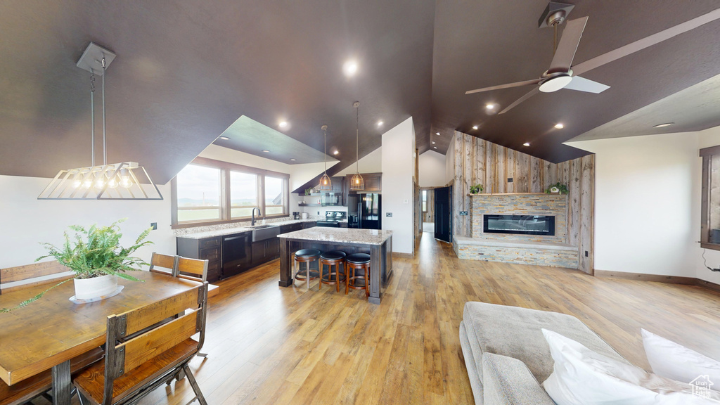 Living room with lofted ceiling, light wood-type flooring, a ceiling fan, a stone fireplace, and baseboards