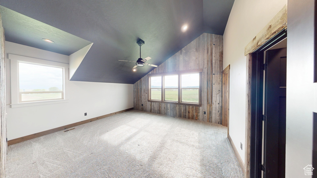 Bonus room featuring vaulted ceiling, a ceiling fan, carpet flooring, baseboards, and wooden walls