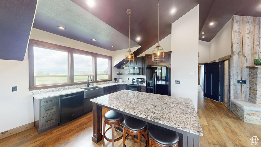 Kitchen featuring black appliances, a sink, light wood-style floors, light stone counters, and recessed lighting