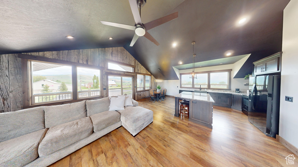 Living area with lofted ceiling, light wood-type flooring, ceiling fan, wooden walls, and recessed lighting