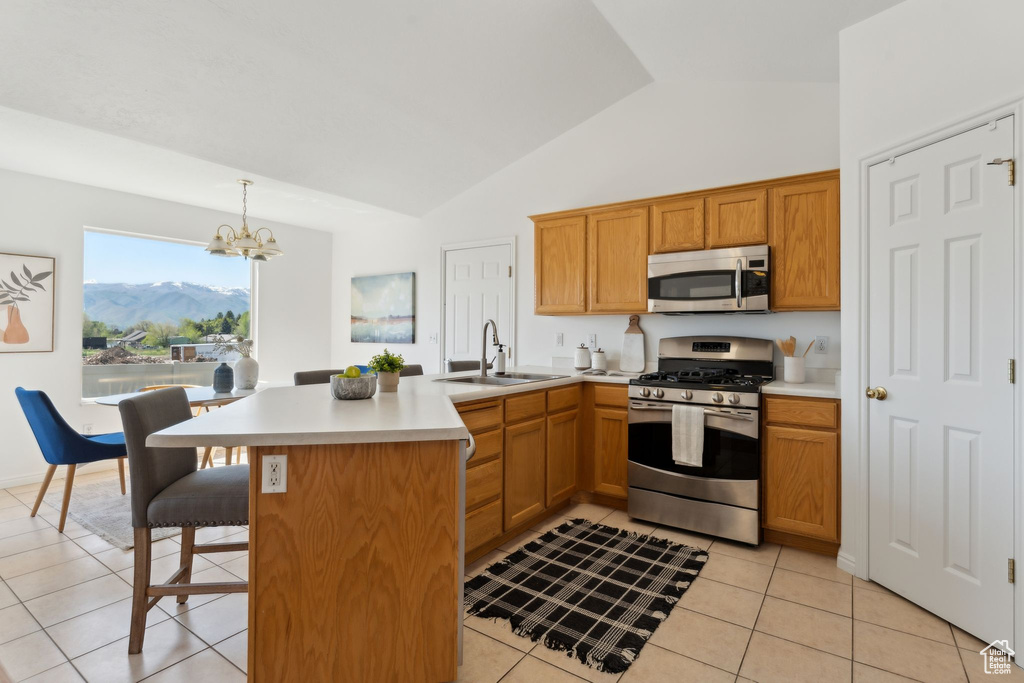Kitchen with stainless steel appliances, a sink, a peninsula, light tile patterned flooring, and high vaulted ceiling